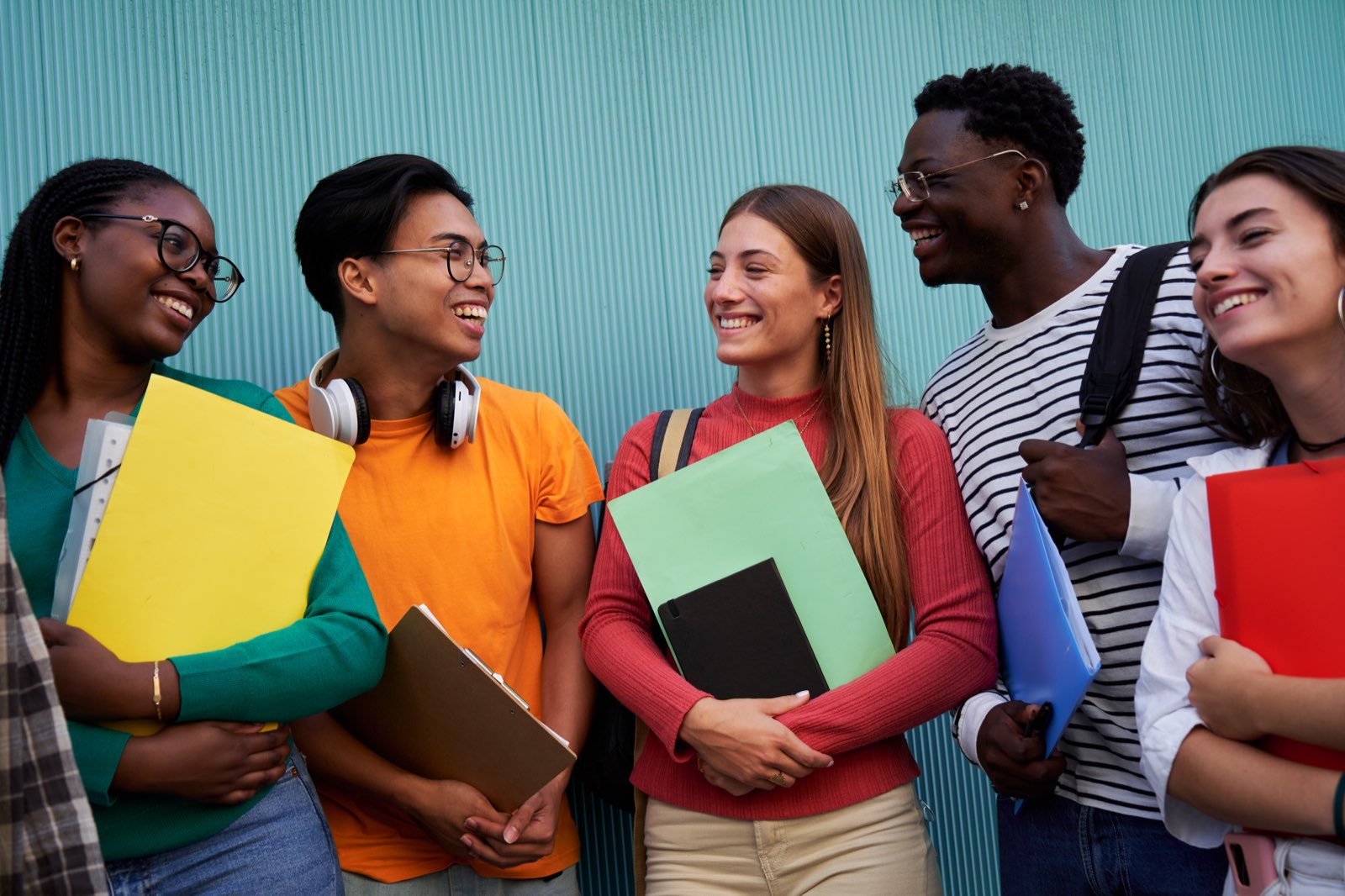 Five students talking together outside school, holding folders and books